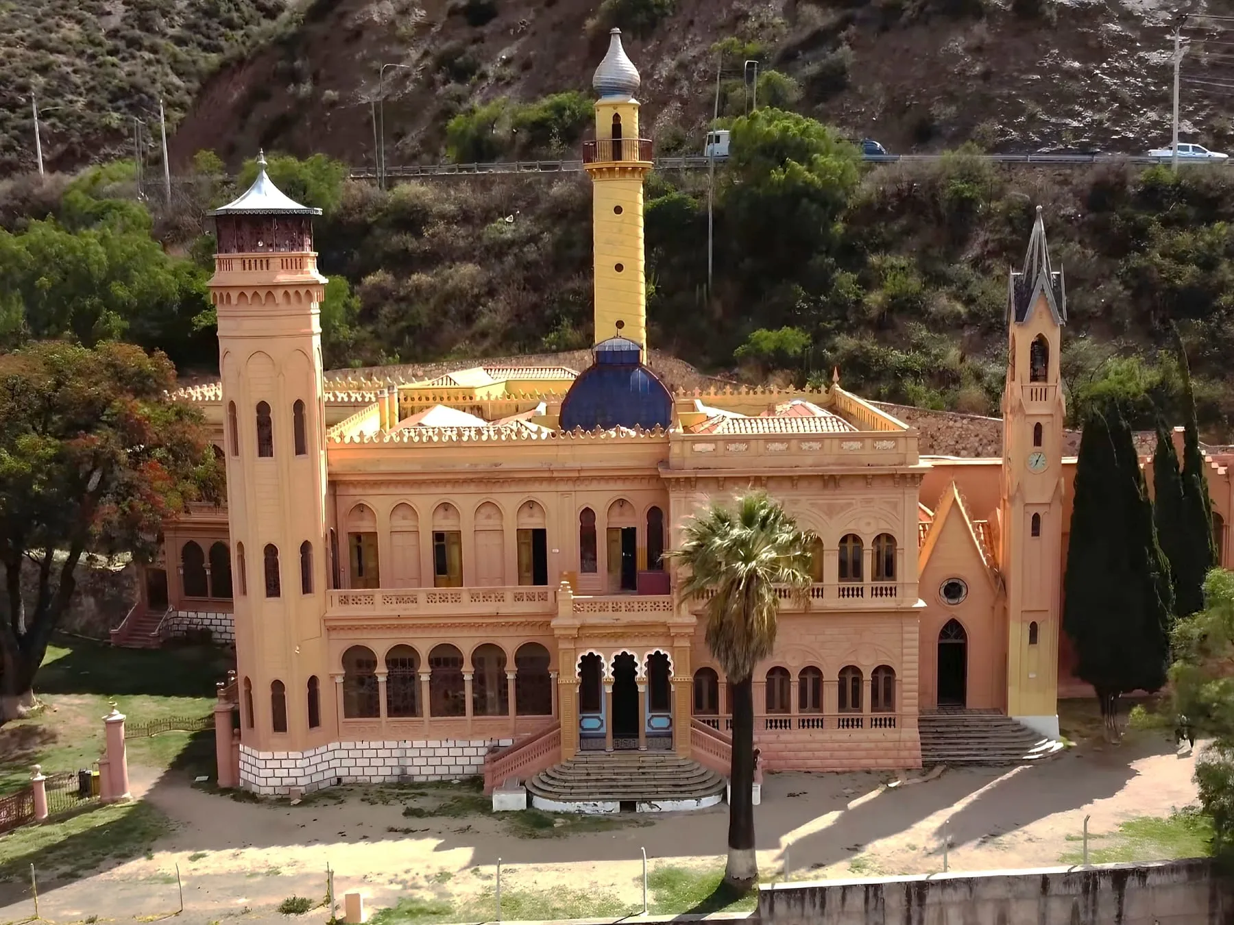Castillo de La Glorieta en Sucre: palacio de fachada rosada con torres de distintos estilos, cúpula azul y minarete amarillo, rodeado de jardines.